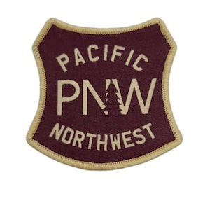 Puede incluir: Un parche de color granate con un contorno blanco y el texto "PACIFIC PNW NORTHWEST" en blanco.