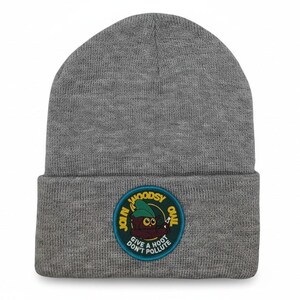 May include: A heather gray knit beanie featuring a circular embroidered patch on the cuff. The patch depicts a brown owl character wearing a green hat, with the yellow and white text "JOIN WOODSY QUAIL" and "GIVE A HOOT DON'T POLLUTE".