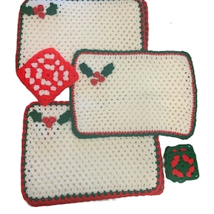 May include: A collection of crocheted Christmas placemats and coasters. The placemats are off-white with red and green trim and holly berry accents. The coasters are red and green square designs.