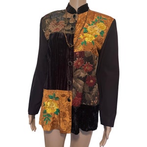 May include: A brown long-sleeved button-up shirt with a patchwork design featuring floral patterns in shades of orange, yellow, green, and red. The shirt has a mandarin collar and a beaded necklace.