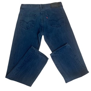 May include: A pair of dark blue denim jeans with a straight leg fit. The jeans have a classic five-pocket design and a leather patch on the back waistband with the Levi's logo.