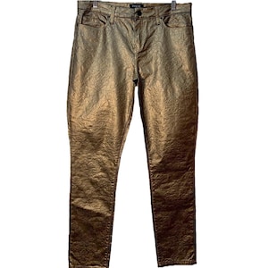 May include: Gold-colored, textured pants with a subtle pattern. The pants have a classic five-pocket design and a button and zipper closure. The brand name "CACHE" is visible on the waistband. These pants are a stylish addition to any wardrobe.