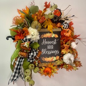 Corona de otoño con flores de otoño, calabaza, cuadros negros de búfalo, puerta y pared.