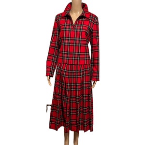 May include: A red and black plaid skirt suit with a zipper closure. The skirt is pleated and the jacket has long sleeves.