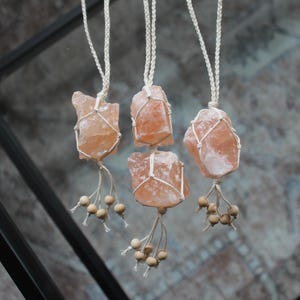 Puede incluir: Cuatro colgantes de cristal de sal rosa del Himalaya colgando de cordones de macram&eacute; blanco con cuentas de madera.