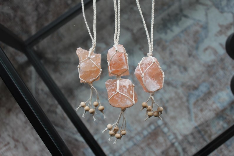 Puede incluir: Cuatro colgantes de cristal de sal rosa del Himalaya colgando de cordones de macram&eacute; blanco con cuentas de madera.