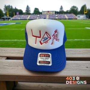 May include: A blue and white trucker hat with the words "Go Rams" and a football player graphic. The hat has a foam front and a mesh back. The hat is sitting on a wooden surface.