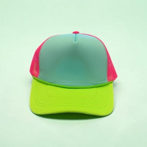 May include: A trucker hat featuring a light blue foam front panel, a bright lime green brim with matching piping, and vibrant pink mesh side and back panels. The cap includes a small pink button at the top center of the crown structure.