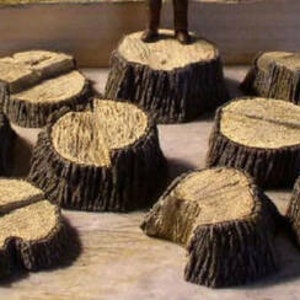 May include: A collection of miniature tree stumps with textured bark and light brown tops. Some stumps have a split or groove across the top. The stumps are arranged on a light-colored surface.
