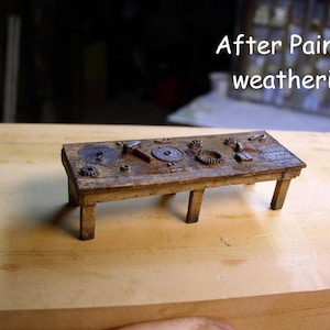 May include: A miniature wooden table with various metal objects on top, including gears and circular pieces. The table has a weathered, aged appearance, with the text "After Paint & weathering" in the upper right corner.