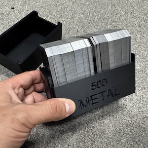 May include: A black plastic case with a metal deck of 500 cards inside. The case has the text "500 METAL" printed on the side.