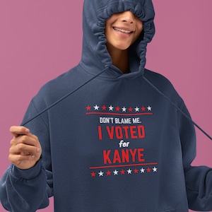 May include: A navy blue hoodie with a red and white graphic that says "Don't blame me. I voted for Kanye." with stars above and below the text.