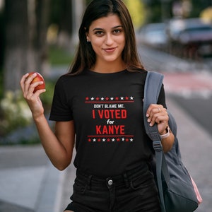 May include: A black t-shirt with a red and white graphic that says "DON'T BLAME ME. I VOTED for KANYE" with stars above and below the text.
