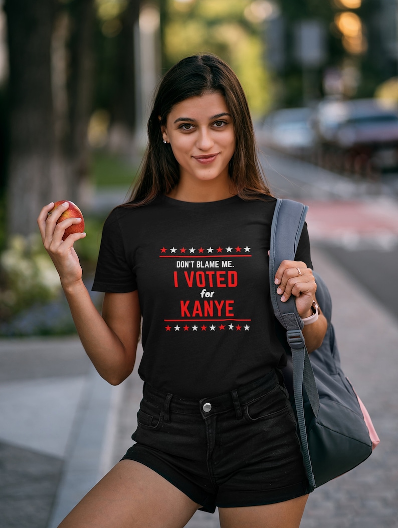 May include: A black t-shirt with a red and white graphic that says "DON'T BLAME ME. I VOTED for KANYE" with stars above and below the text.