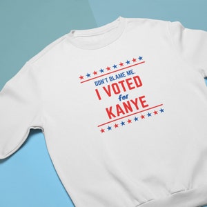 May include: White sweatshirt with red and blue text that reads "Don't blame me. I voted for Kanye" surrounded by red and blue stars.