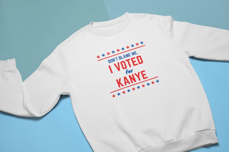 May include: White sweatshirt with red and blue text that reads "Don't blame me. I voted for Kanye" surrounded by red and blue stars.