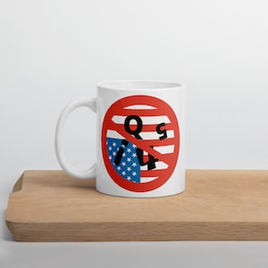 May include: White ceramic mug with a red circle and diagonal line through it. The circle has a red, white, and blue American flag design with the letters "Q" and "S" on either side of the line.