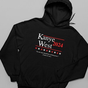 以下が含まれることがあります： 「Kanye West 2024」と「No one man should have all that power. (Unless it's me.)」という白いプリントが施された黒いフード付きスウェットシャツ。テキストの両側に赤い星が5つずつあります。