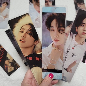 May include: A selection of rectangular bookmarks featuring images of a person. The bookmarks are in clear plastic sleeves. Some bookmarks have text that reads "Stray Kids" and "MAXIDENT MINI ALBUM".