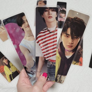 May include: A collection of clear plastic bookmarks featuring images of young men. The bookmarks have a black section at the bottom. The men are wearing various outfits, including a striped shirt and a yellow jacket.