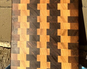 May include: A large, rectangular cutting board made of wood with a checkerboard pattern of light and dark wood. The board is made of walnut and maple wood.