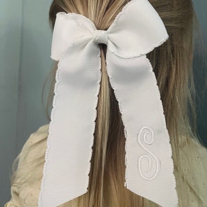 K&ouml;nnte beinhalten: Wei&szlig;es Satin-Haarband mit gewelltem Rand und einem wei&szlig;en gestickten Buchstaben "S" auf einer Seite.