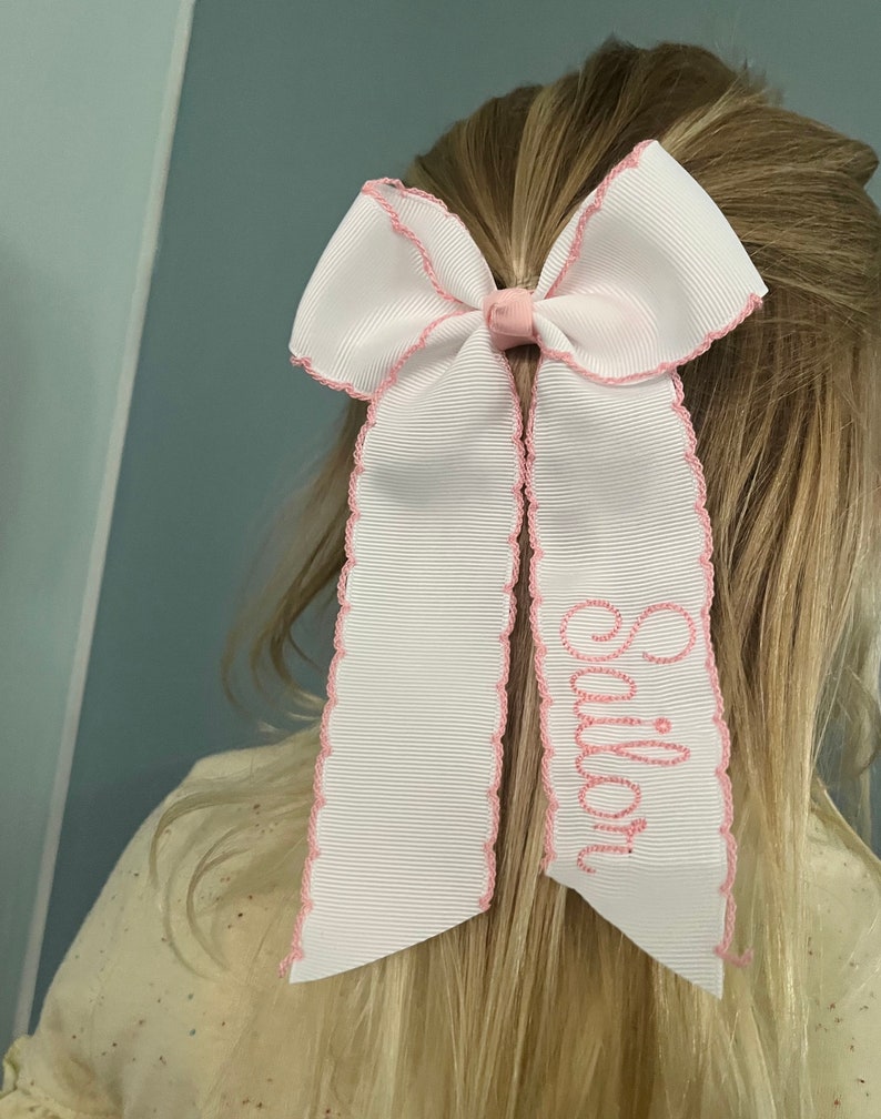 K&ouml;nnte beinhalten: Wei&szlig;er Haarreifen mit rosa Besatz und dem Wort "Emily" auf einer Seite gestickt.