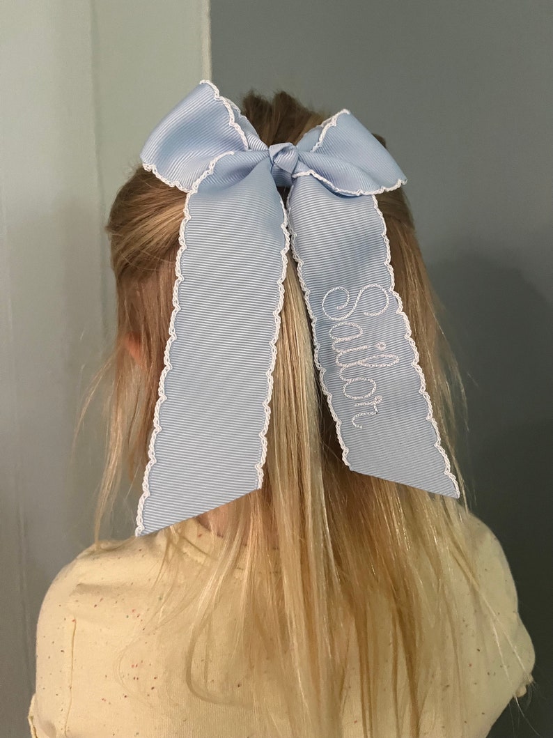 K&ouml;nnte beinhalten: Ein hellblaues Haarband mit wei&szlig;en gewellten R&auml;ndern und dem Namen "Sullivan" in wei&szlig; auf einer Seite gestickt.