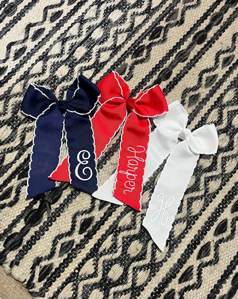 K&ouml;nnte beinhalten: Drei Haarb&auml;nder mit gewellten R&auml;ndern und personalisierter Stickerei. Die Schleifen sind marineblau, rot und wei&szlig;. Die marineblaue Schleife hat den Buchstaben "E" gestickt, die rote Schleife den Namen "Harper" gestickt und die wei&szlig;e Schleife den Buchstaben "H" gestickt.