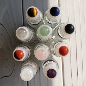 May include: A collection of eight glass roller bottles with different colored gemstone tops. The gemstones include tiger's eye, lapis lazuli, black onyx, amethyst, rose quartz, red jasper, aventurine, and clear quartz.