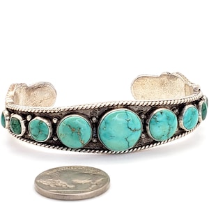 May include: A silver cuff bracelet with turquoise stones set in a silver band. The bracelet is about the size of a US dime.