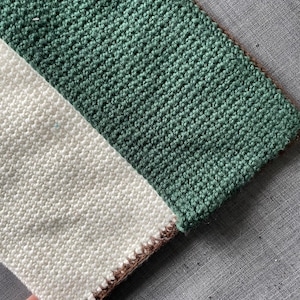 May include: A crocheted scarf with a white and green striped pattern. The scarf has a brown border.