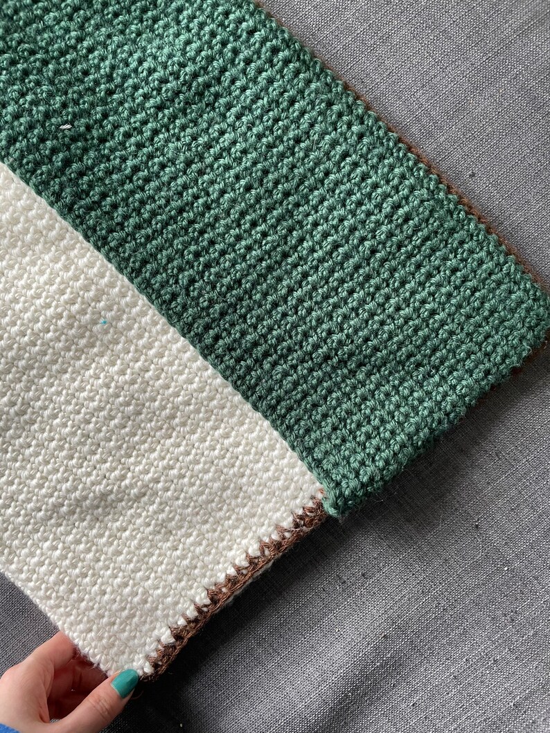 May include: A crocheted scarf with a white and green striped pattern. The scarf has a brown border.