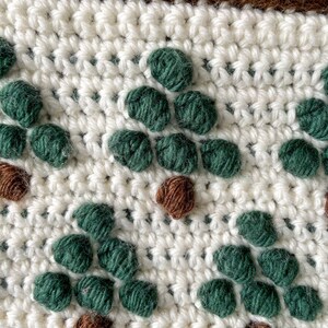 May include: Close-up of a crocheted fabric with a repeating pattern of green and brown yarn circles. The fabric is white and has a brown border.