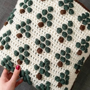 May include: A white crocheted pillow with a repeating pattern of green and brown circles. The pillow has a brown border.