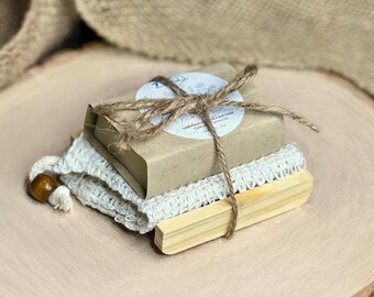 May include: A brown and white bar soap wrapped in brown paper with twine and a white label that says "Handmade Sea Salt Soap". The soap is sitting on a white mesh bag and a wooden soap dish.