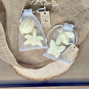 Könnte beinhalten: Zwei kleine weiße Organzasäckchen gefüllt mit kleinen weißen Seifen-Geschenken in Form eines Schmetterlings, einer Libelle und einer Biene. Die Säckchen haben Dankeschön-Etiketten mit dem Text "Vielen Dank" und "Sarah's Baby Shower 06.20.2023" angebracht.