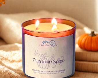 May include: A three-wick candle in a translucent amber glass jar with a white label. The label features a dragonfly logo, the text Wild Karma Candle Co., Pumpkin Spice, and Beeswax and Essential Oils Candle, Hand-Poured in Melbourne FL 16 oz.