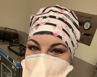 Könnte beinhalten: Eine Frau trägt eine blaue OP-Hose mit einer Anstecknadel mit dem Logo der Kansas City Chiefs. Sie trägt auch eine rosa-schwarze OP-Mütze und eine hellrosa OP-Maske mit blauem Rand. Die Maske trägt den Schriftzug "GRAYANO".