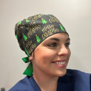 May include: A black scrub hat with a green and gold pattern of Christmas trees and the text "Merry Christmas".