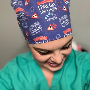May include: A blue scrub hat with a white and red pattern. The hat has the text "WARNING! I PASS GAS FOR A LIVING #ANESTHESIA" repeated on it.