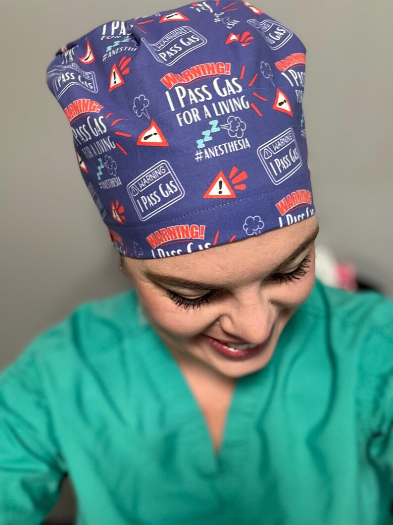 May include: A blue scrub hat with a white and red pattern. The hat has the text "WARNING! I PASS GAS FOR A LIVING #ANESTHESIA" repeated on it.