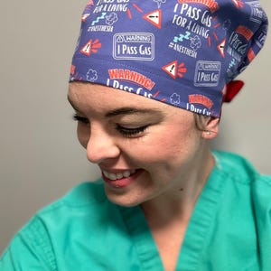 May include: A blue scrub hat with a red and white pattern. The hat has the text "I Pass Gas for a Living" and "#Anesthesia" printed on it.