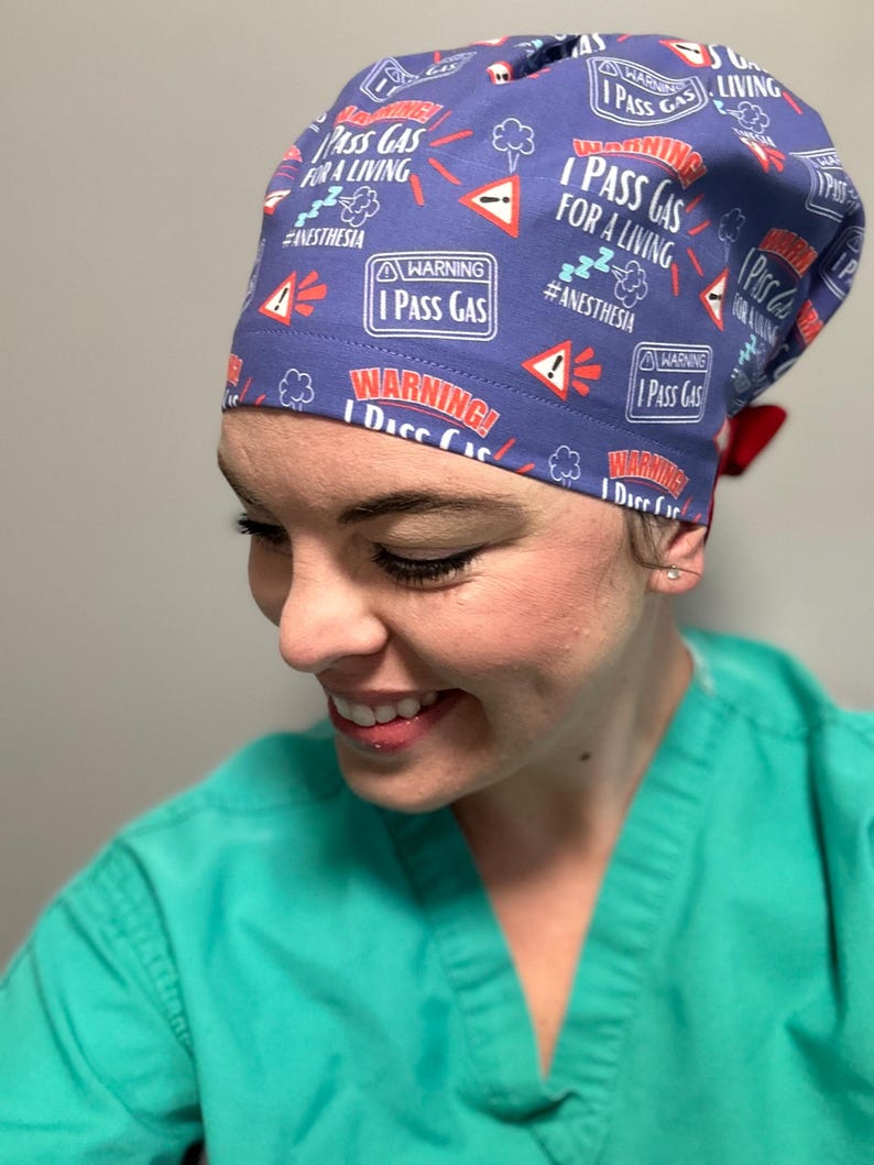 May include: A blue scrub hat with a red and white pattern. The hat has the text "I Pass Gas for a Living" and "#Anesthesia" printed on it.