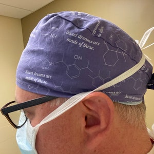 May include: A purple surgical scrub hat with a white tie. The hat has a white print of chemical structures and the text "Sweet dreams are made of these."