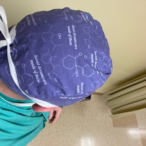 May include: A purple surgical scrub hat with a white tie. The hat has a repeating pattern of chemical structures and the text "Sweet dreams are made of these."