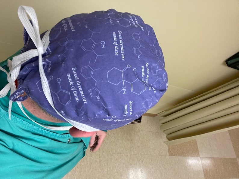 May include: A purple surgical scrub hat with a white tie. The hat has a repeating pattern of chemical structures and the text "Sweet dreams are made of these."