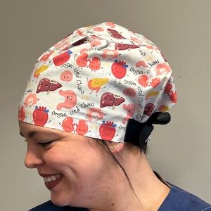 May include: A white scrub hat with a colorful print of cartoon organs and the text "Organ-ized Chaos".