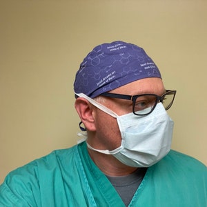 May include: A person wearing a purple surgical scrub hat with a white chemical structure and the text "Sweet dreams are made of these." The person is also wearing a blue surgical mask and black framed glasses.