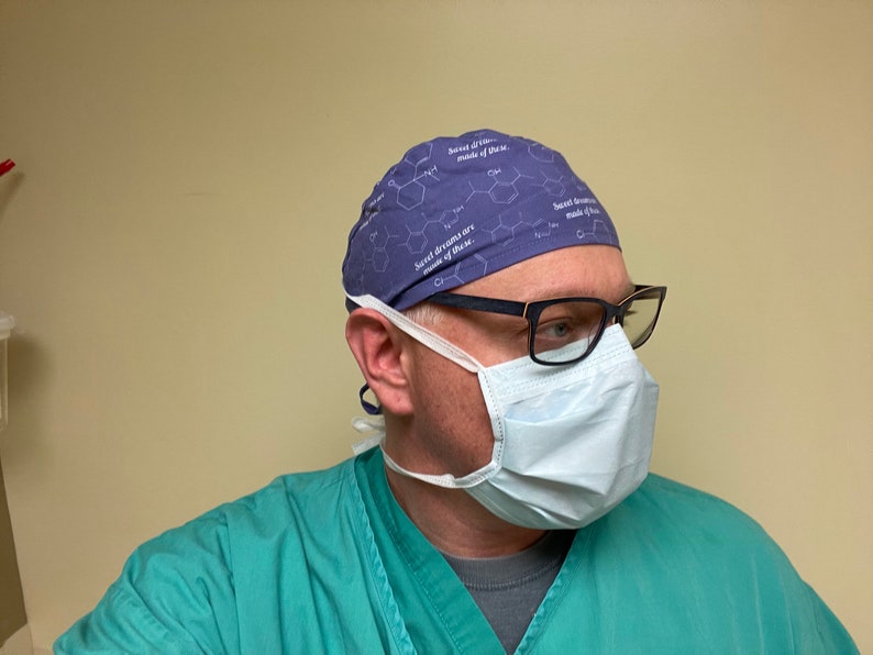 May include: A person wearing a purple surgical scrub hat with a white chemical structure and the text "Sweet dreams are made of these." The person is also wearing a blue surgical mask and black framed glasses.